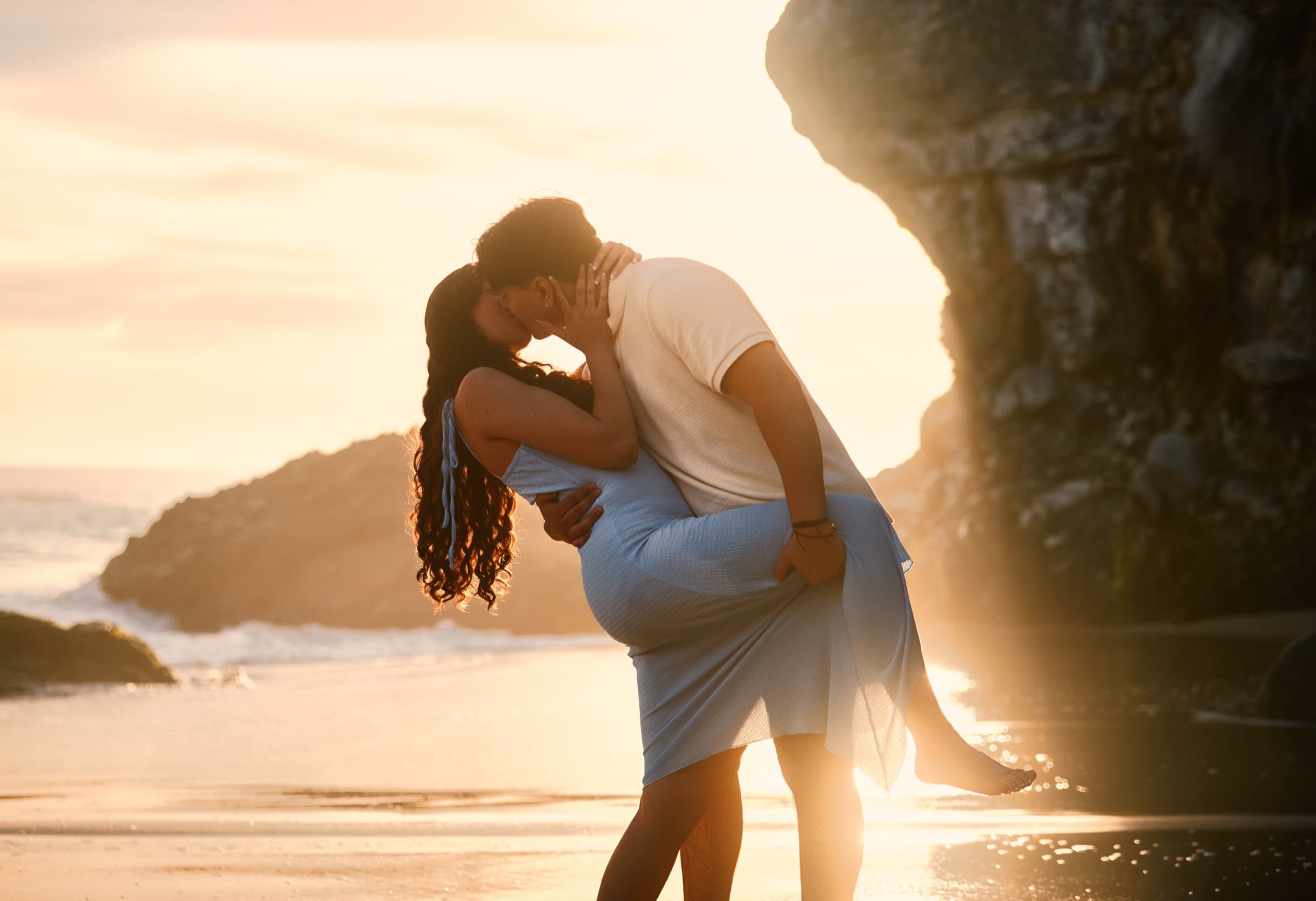 Couple kissing in golden-hour sun flare on the beach